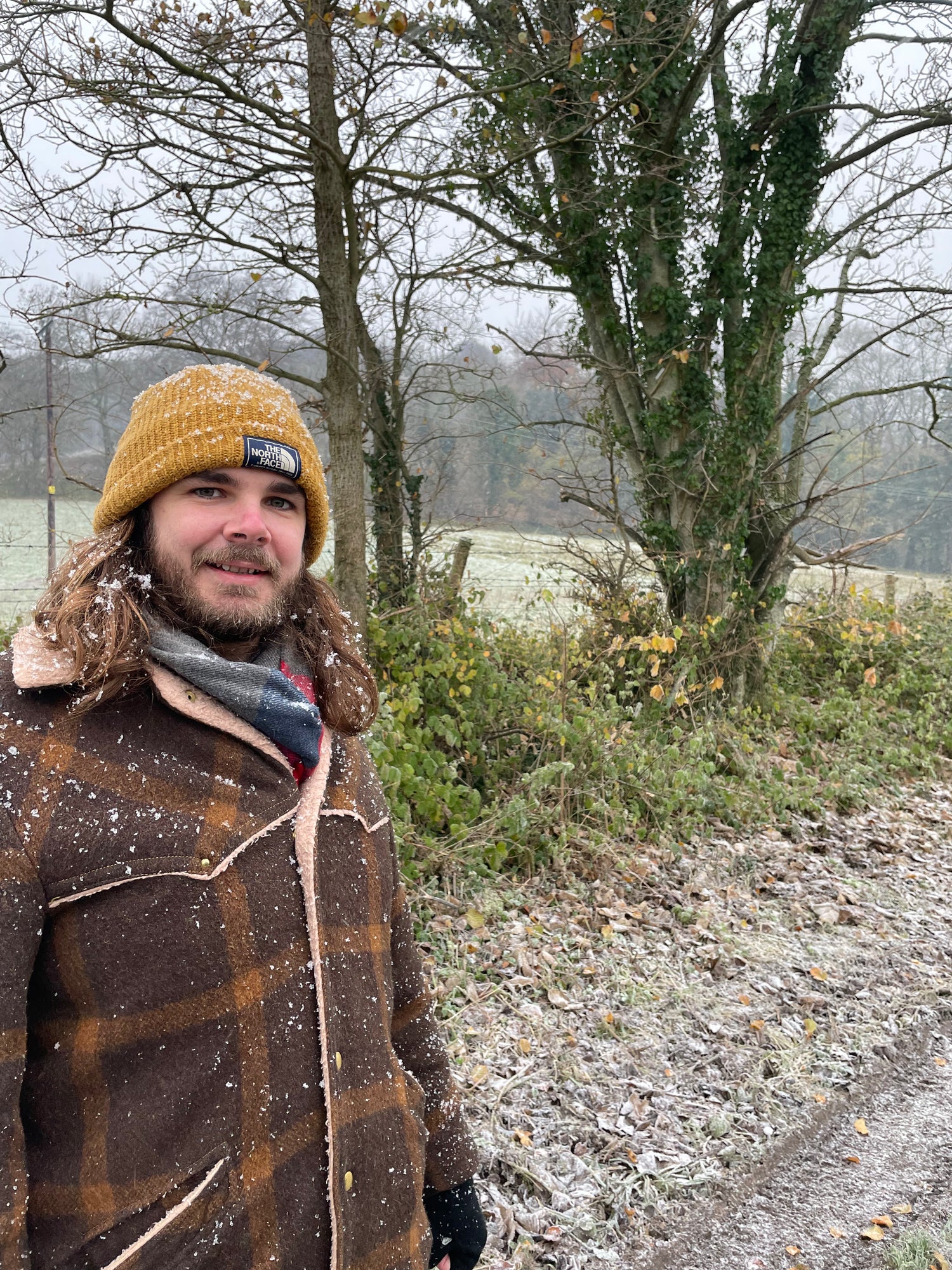 Man in winter clothing standing on a snowy path with trees in the background